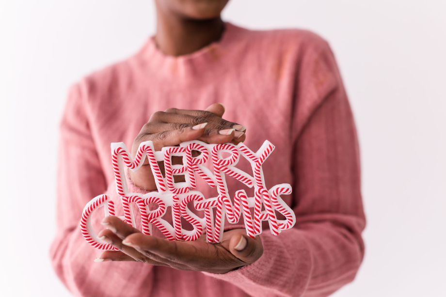 Women holding merry christmas sign while wearing a holiday sweatshirt.